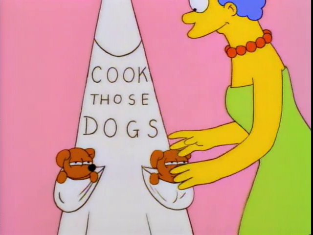 Marge Simpson next to an apron that says "COOK THOSE DOGS" with two puppies in the pockets